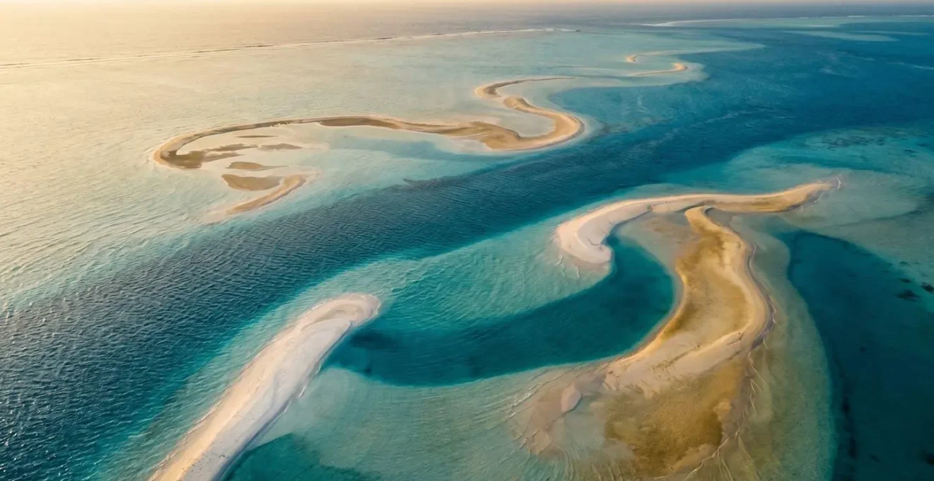 Vue aérienne minimaliste d'un lagon aux eaux cristallines avec jeux de lumière naturels révélant les bancs de sable