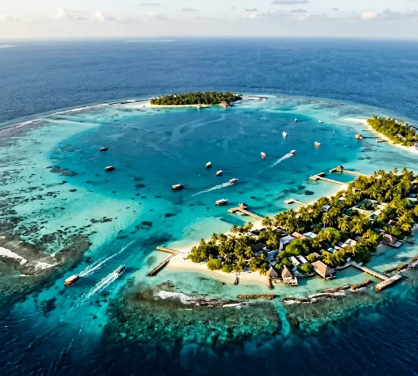 Vue aérienne d'un atoll maldivien montrant le contraste entre les îles locales habitées et les lagons turquoise, avec des dhonis traditionnels naviguant entre les îles