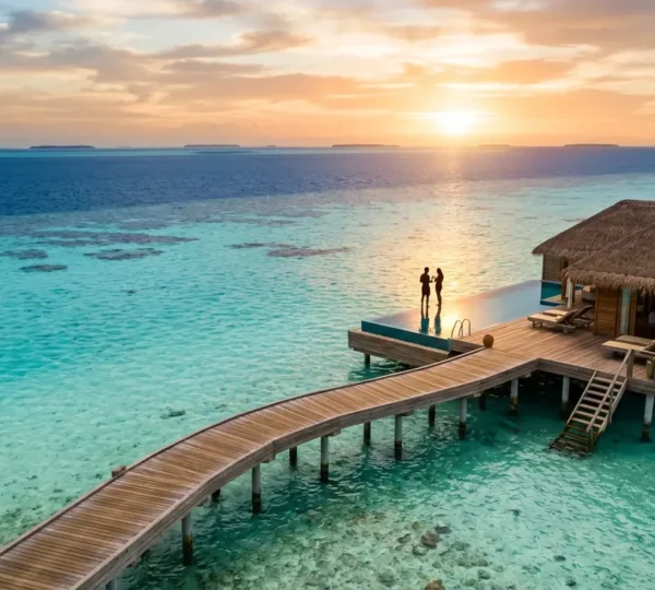 Vue aérienne romantique d'une villa sur pilotis aux Maldives au coucher du soleil avec un couple sur la terrasse