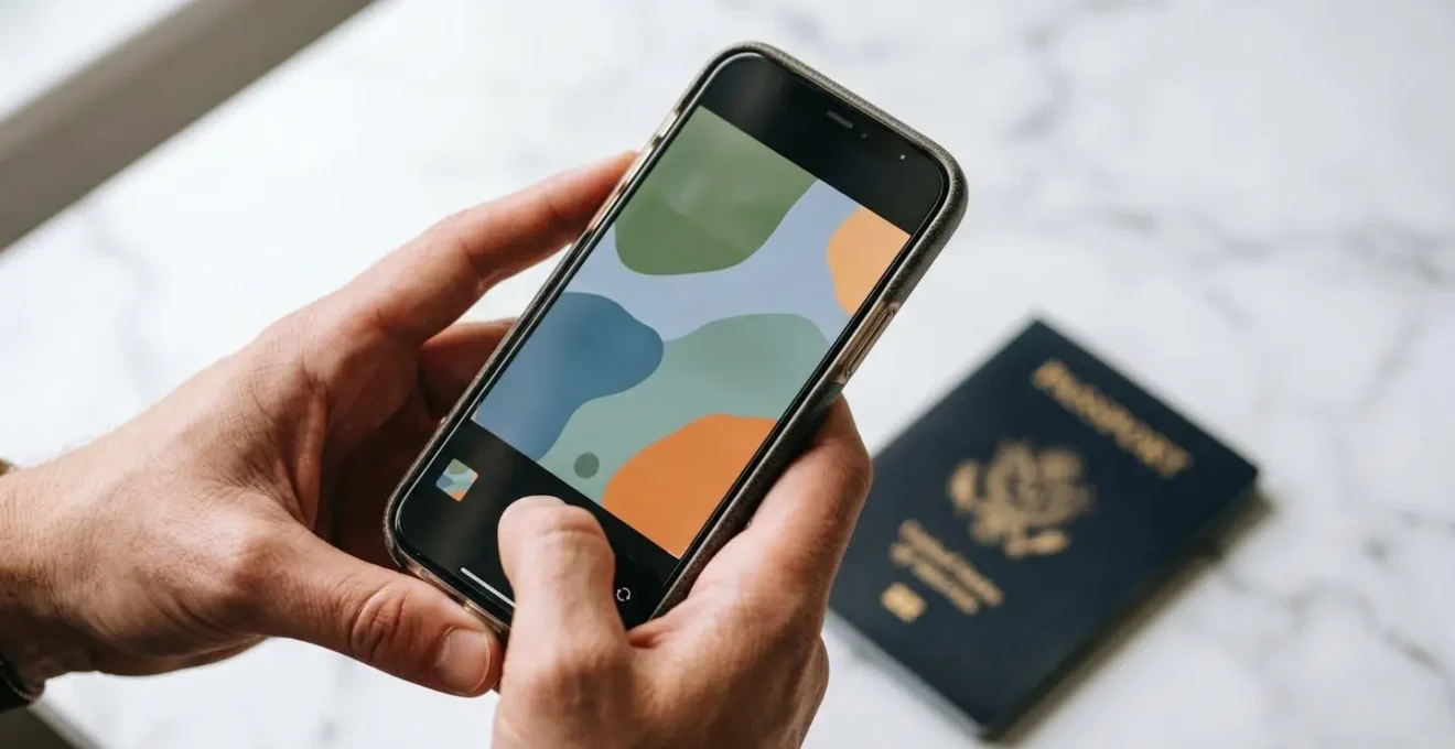 Mains tenant un smartphone photographiant un passeport posé sur une surface claire avec lumière naturelle douce