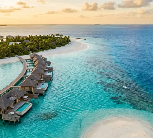 Vue aérienne d'un resort aux Maldives avec ses bungalows sur pilotis et ses eaux cristallines, illustrant le paradis tropical et son coût réel
