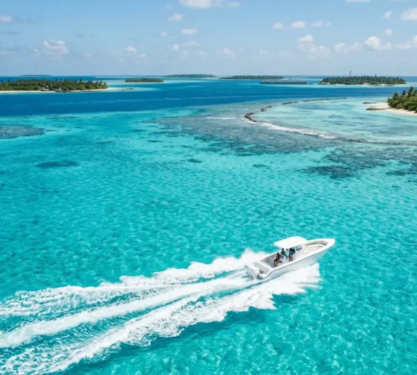 Vue aérienne d'un speedboat blanc naviguant sur les eaux turquoise cristallines des Maldives avec des îles en arrière-plan
